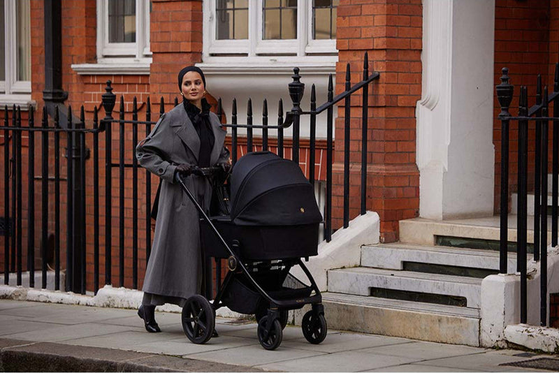Woman pushing a black stroller in front of a brick building